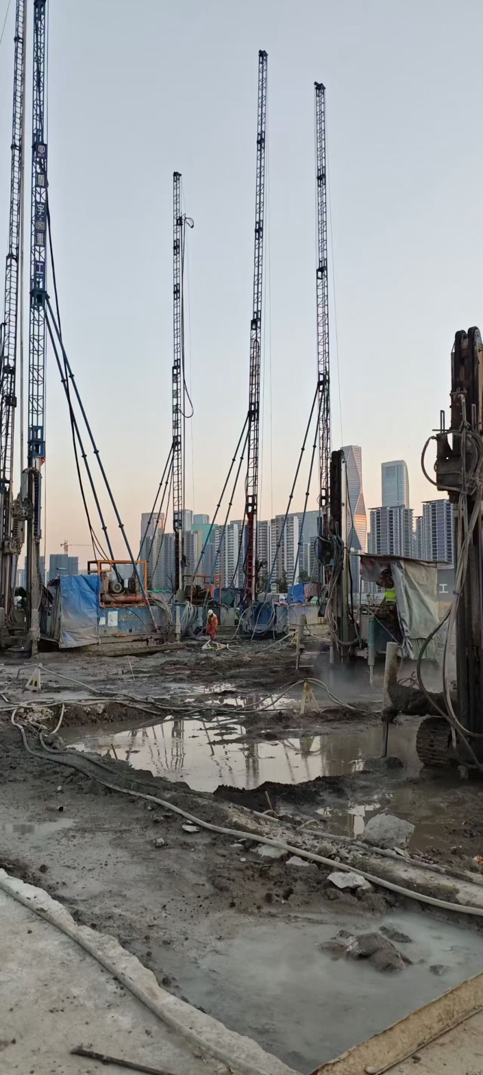 Rigs standing on a muddy site in front of a city skyline